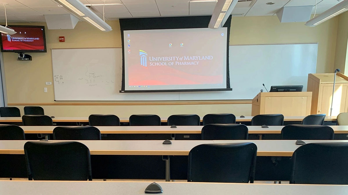 Classroom in Pharmacy Hall North with rows of desks and chairs facing a projection screen and instructor podium.